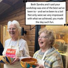 Load image into Gallery viewer, Two older adults enjoying a vintage wooden bowl upcycling workshop, smiling and holding up their bowls.