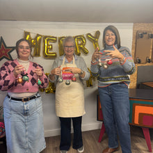 Load image into Gallery viewer, Three people holding ceramic christmas baubles they have just painted
