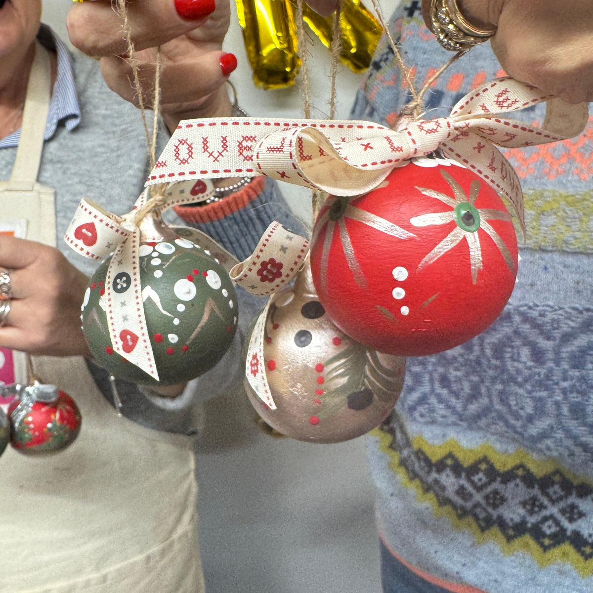 Close-up of hands holding Christmas ornaments with a colorful sweater in the background