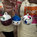 Three hand-painted Christmas ornaments  The ornaments include a green holiday design, a snowman face with a blue hat, and a white ornament with black and blue details.