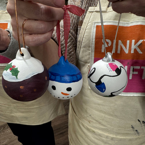Three hand-painted Christmas ornaments  The ornaments include a green holiday design, a snowman face with a blue hat, and a white ornament with black and blue details.