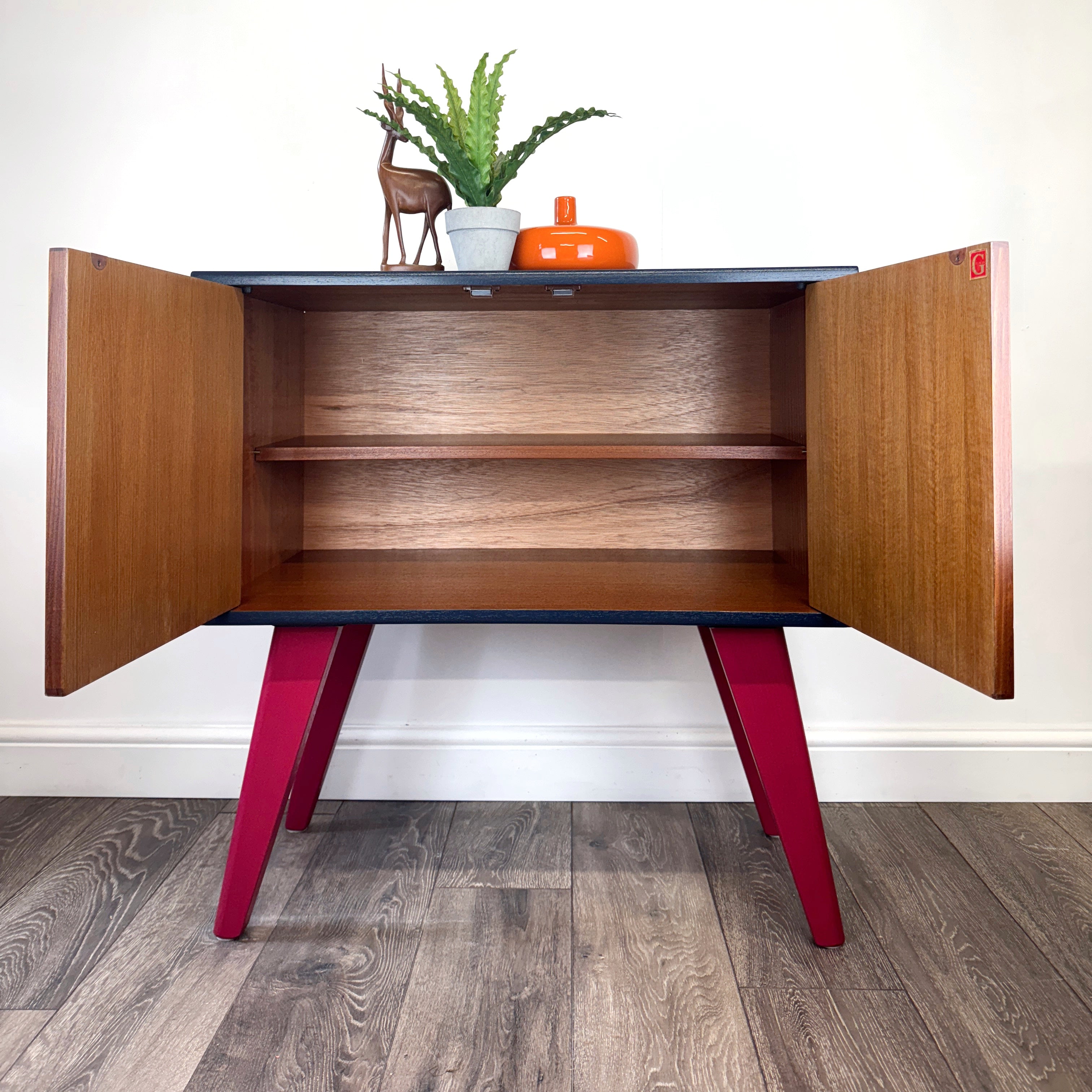 Colorful G Plan cabinet handpainted with abstract design on a wooden floor with it's doors open