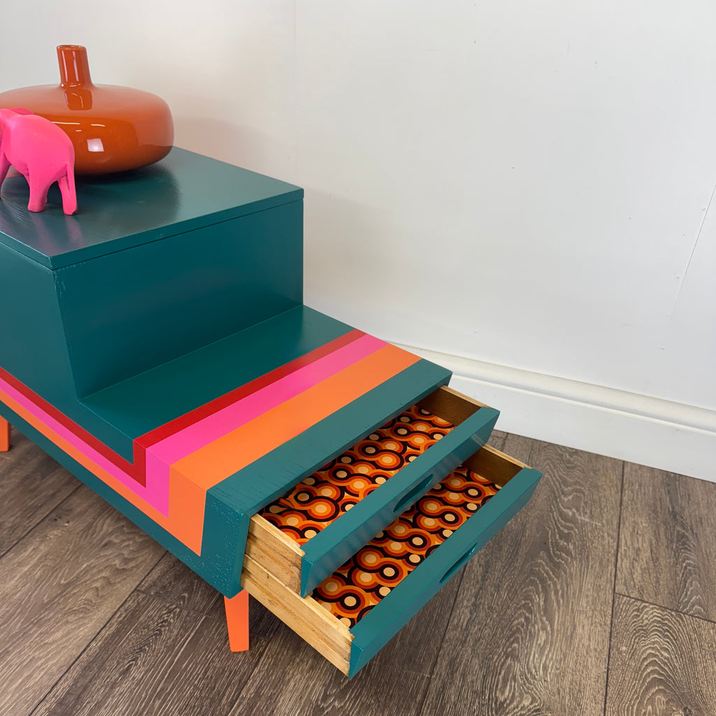 Colorful striped mid century sewing box with a pink elephant figurine on a plain background