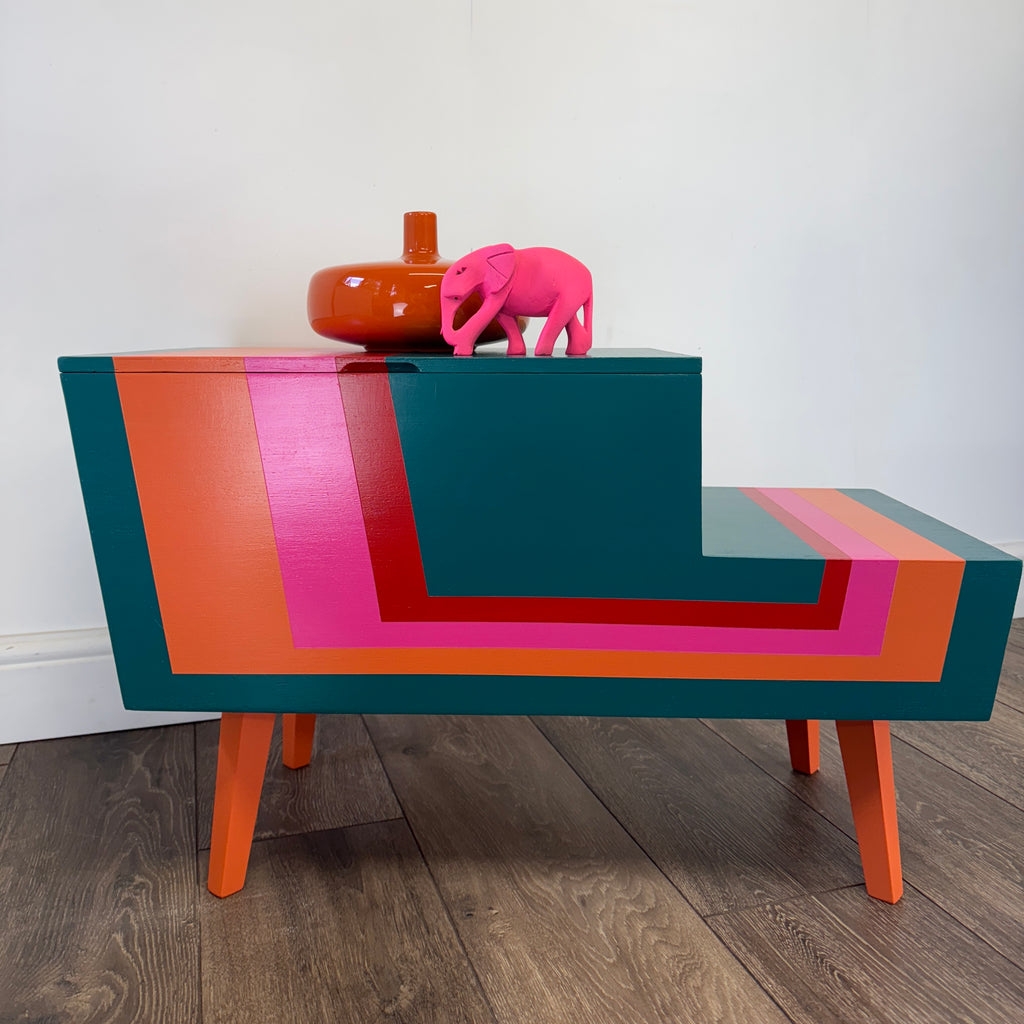 Colorful striped mid century sewing box with a pink elephant figurine on a plain background
