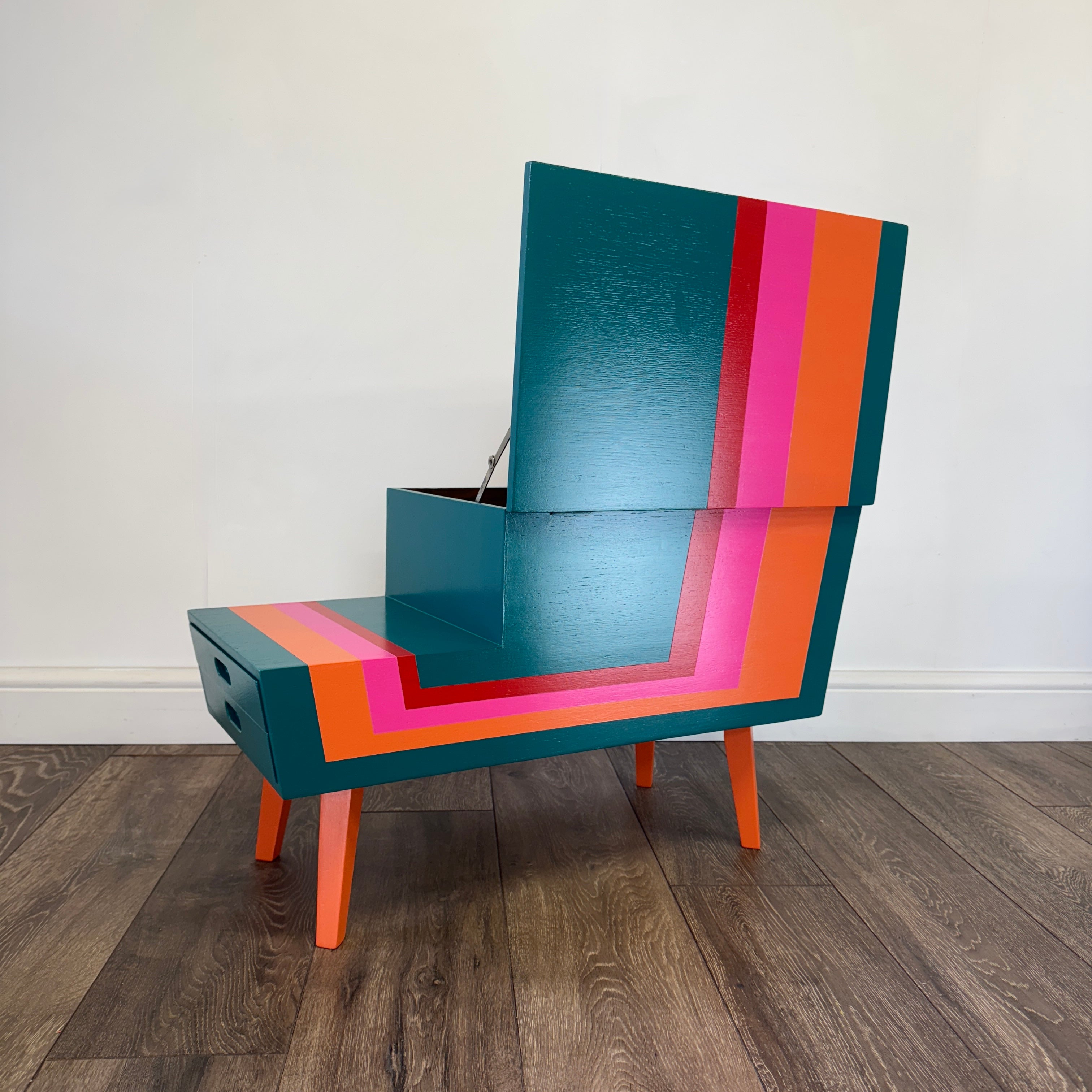 Colorful striped mid century sewing box with a pink elephant figurine on a plain background